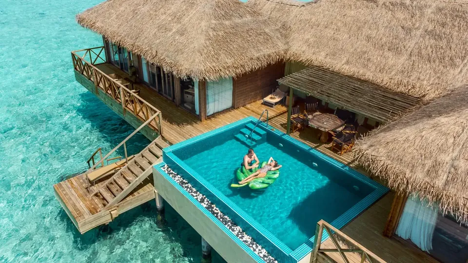 An overwater villa with a private pool and a thatched roof above clear water
