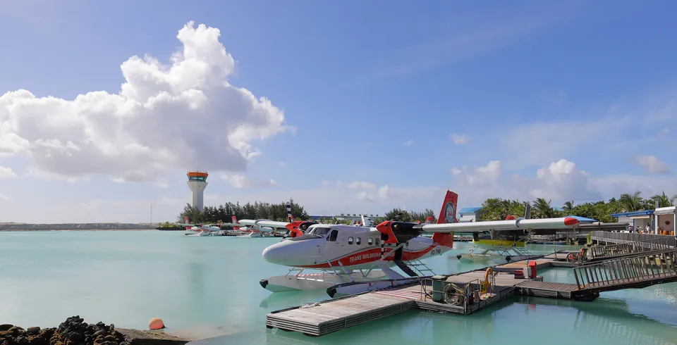 Seaplanes moored at the seaplane terminal beside Velana International Airport, with turquoise water and a clear sky