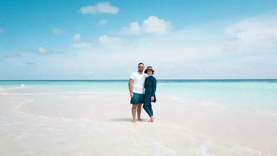 A couple walking hand in hand on a white beach beside a turquoise sea