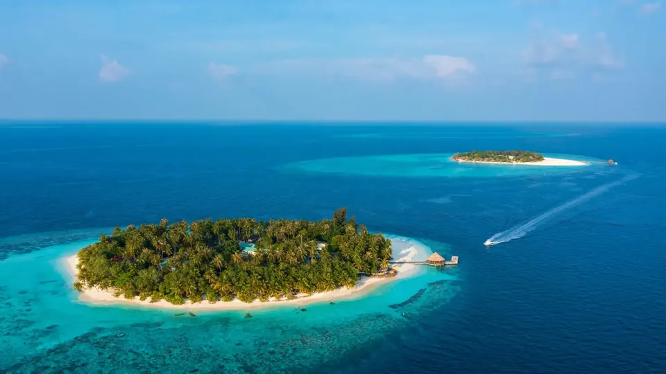 Luftaufnahme einer kleinen grünen Resortinsel mit weißem Sandstrand und türkisfarbener Lagune