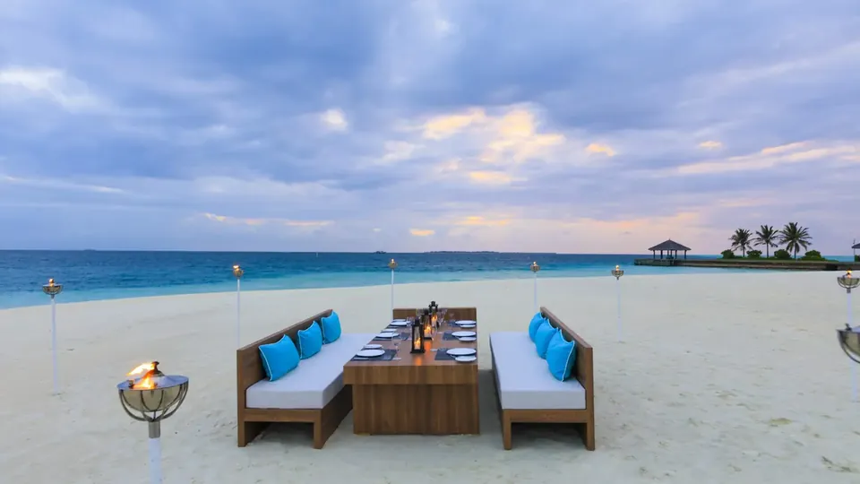 A private dining set-up with sofas and lanterns on a white beach by the sea