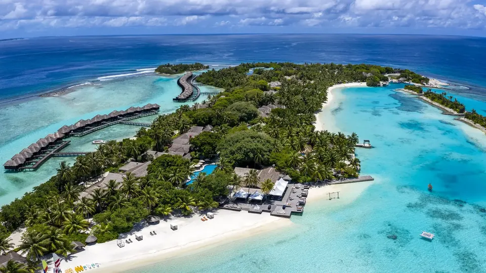 Aerial view of a green resort island with a white beach, a lagoon and a row of overwater villas