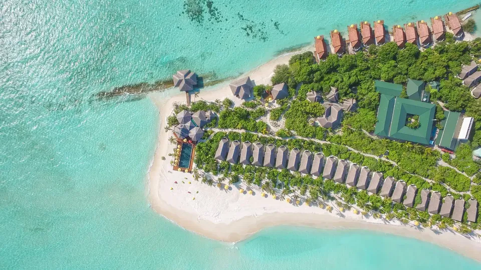 Aerial view of a small resort island with beach villas, a pool and a turquoise lagoon