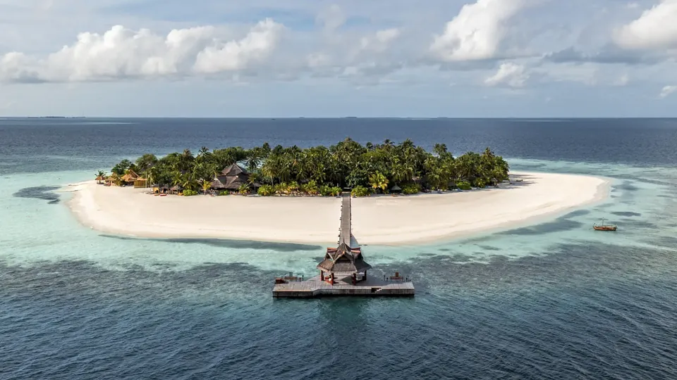 A small round island with palm trees and a white beach surrounded by a turquoise lagoon