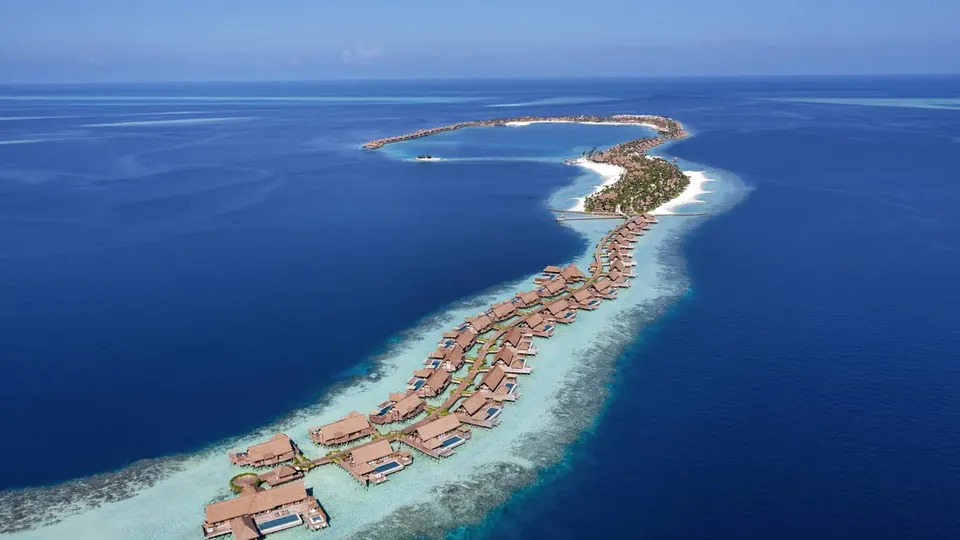A long curved island with rows of villas along a reef in deep blue sea