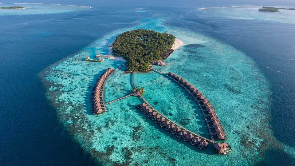 Uma ilha remota com um resort e vilas sobre a água, cercada por recifes e pelo azul profundo do oceano