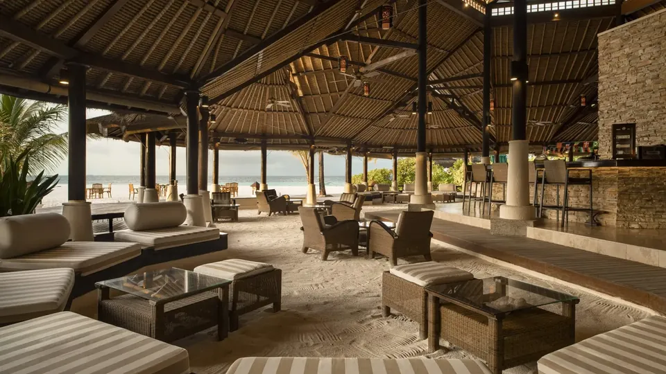 Restaurante de resort aberto para a praia, com sofás e mesas