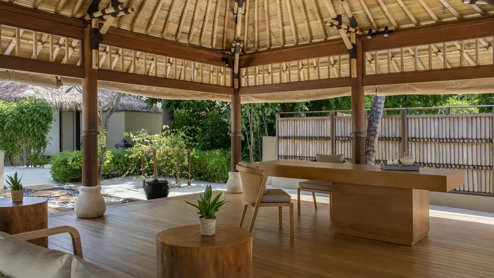 Pavilhão de spa aberto, com teto de palha, cercado por um jardim tropical