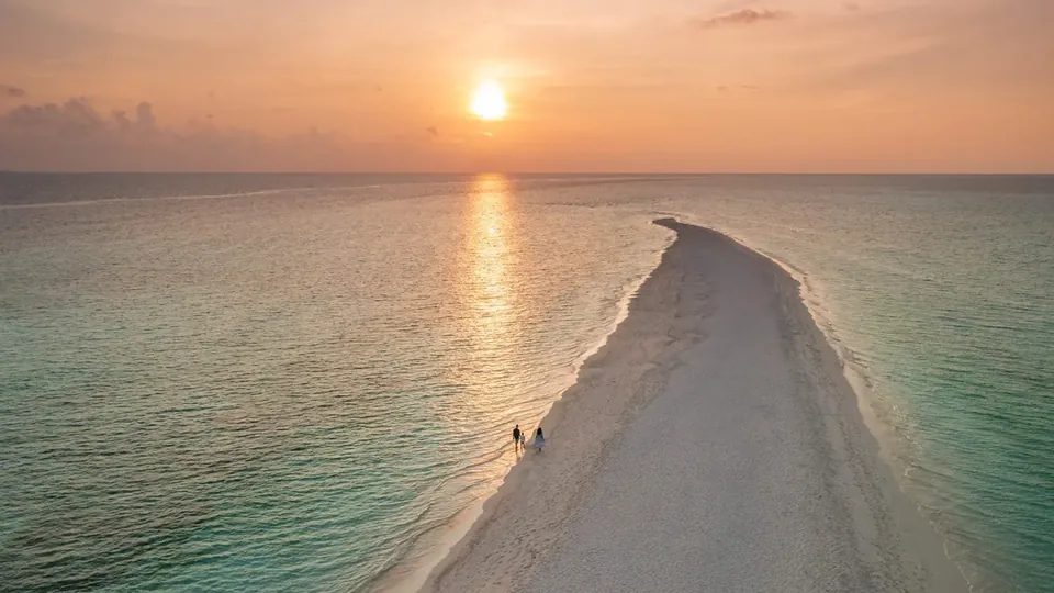 Um banco de areia longo e estreito que se estende pela lagoa ao pôr do sol, com duas pessoas caminhando sobre ele