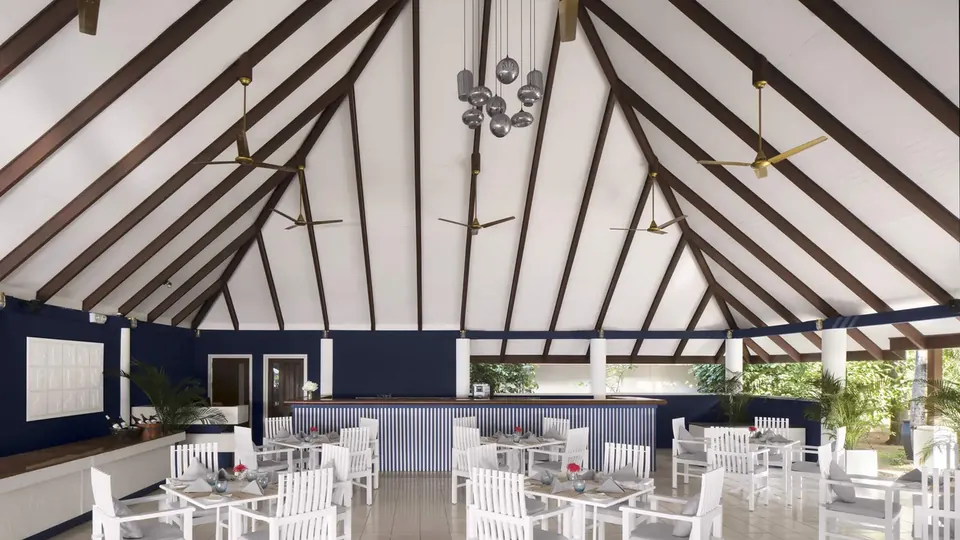 A bright open-sided pavilion with a high wooden roof and tables set for guests