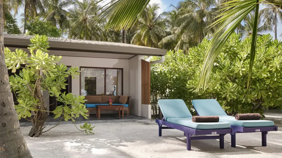 A beach villa with a shaded terrace and loungers under palms