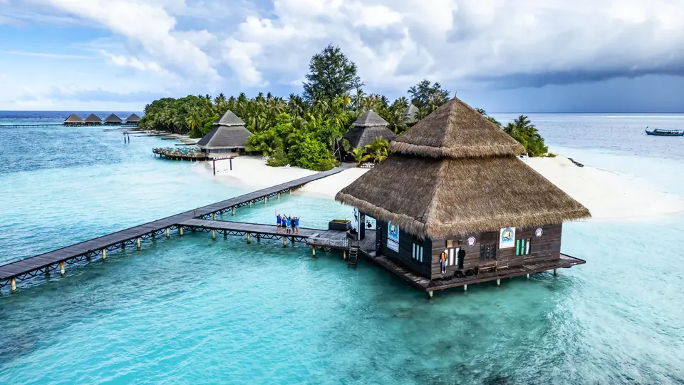 A thatched overwater villa on a wooden jetty above a clear turquoise lagoon