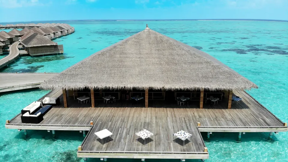 A wooden overwater pavilion with a thatched roof above a clear lagoon